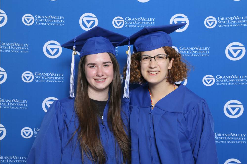 Two friends pose together wearing their cap and gowns at Gradfest